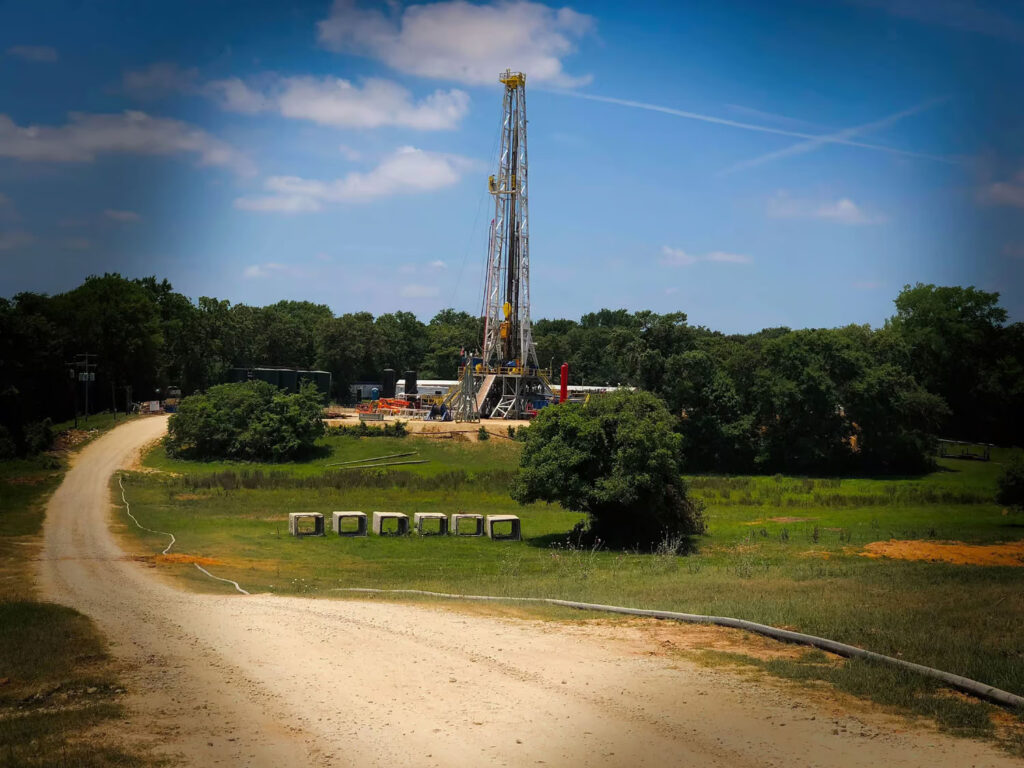 Oil drilling rig in rural landscape with trees and blue sky.