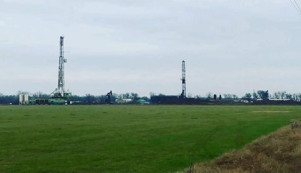 Oil drilling rigs in a green field under a cloudy sky.