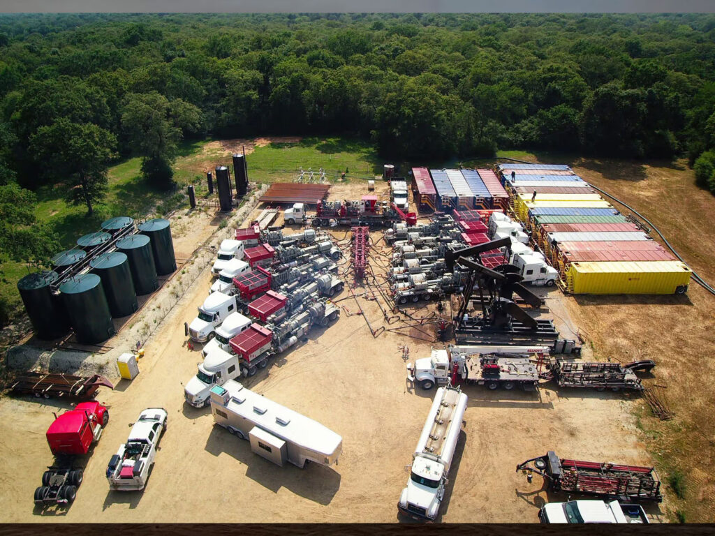 Aerial view of an industrial drilling site with trucks, containers, and machinery.