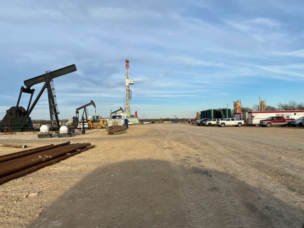 Oilfield site with drilling rigs, trucks, and construction equipment under a blue sky.